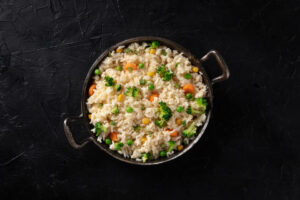 pan of white rice and vegetables sitting on black surface