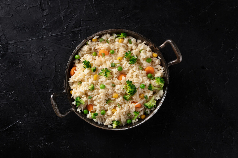 pan of white rice and vegetables sitting on black surface