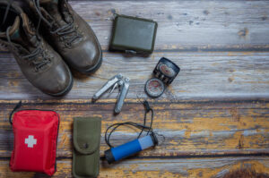 boots, first aid kit, compass, and other survival gear on a wooden surface