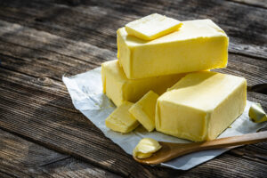 fresh sticks of butter sitting on paper wrapping on a wood surface with a small wood spoon