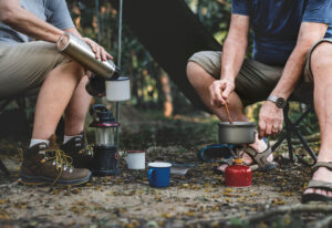 two people sitting in camping chairs cooking in a small pan over a portable stove in the outdoors